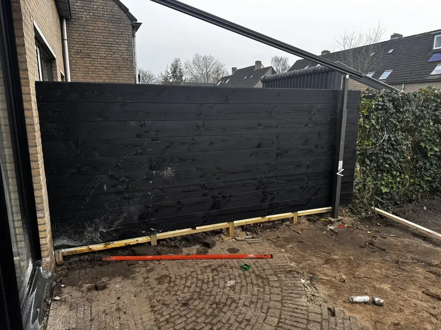 Een nieuwe zwarte houten schutting naast het huis