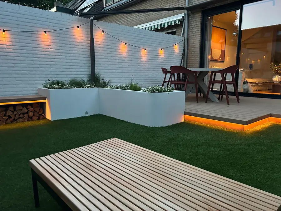 Vanaf de loungeset: beplante plantenbakken, lichtsnoeren en ledverlichting onder de vlonder en het bankje