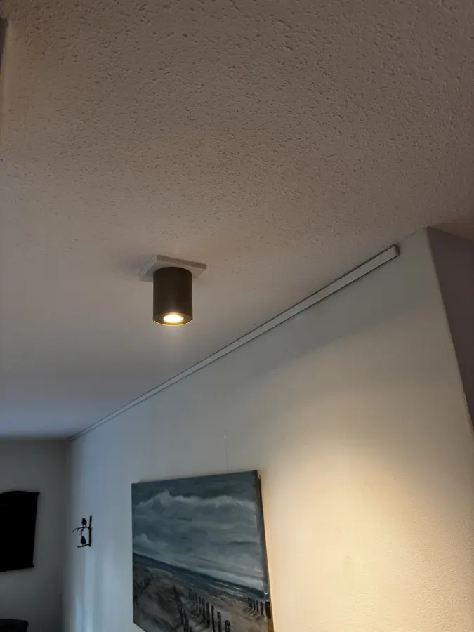 Een nieuwe opbouwspot op een witte afdekplaat, naast de gordijnrail